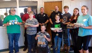 Five boys and three girls holding trays of cupcakes and cookies. Two police officers are standing in the center of the group.
